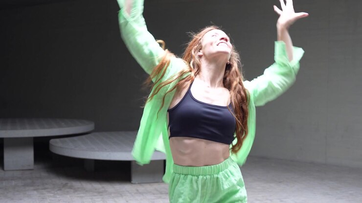 A young woman in green outfit dances outdoors with a joyful and energetic expression