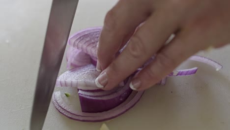 A-women-slicing-a-red-onion-on-a-white-chopping-board-with-a-sharp-knife