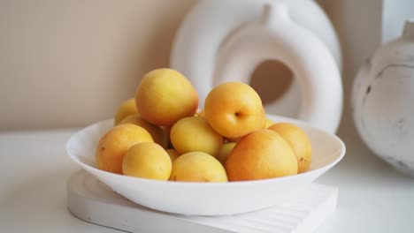 a bowl of ripe yellow plums on a white table