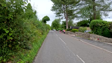 a vehicle travels down a quiet, tree-lined road in the english countryside, passing traffic cones and barriers under overcast daylight with steady forward camera movement