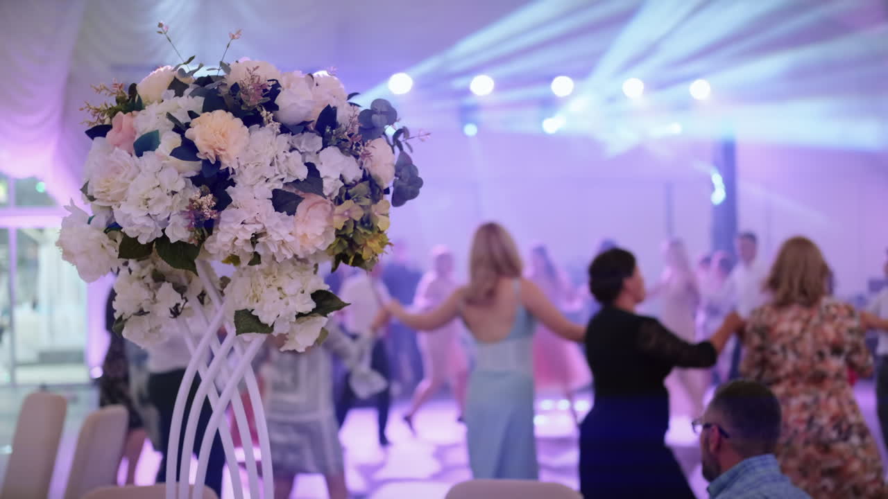 Guests dancing moldavian national dance - Hora at a wedding. Bouquet on the foreground. Stage lights