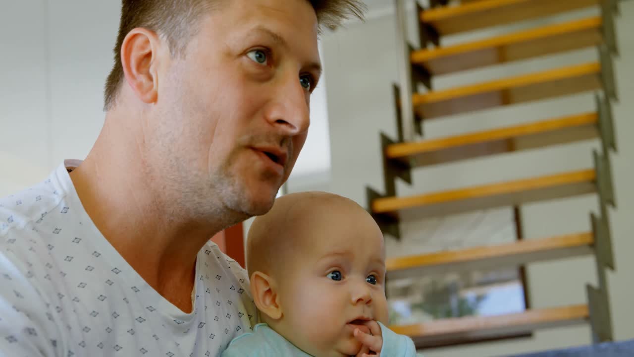 Father and baby boy watching television in living room 4k