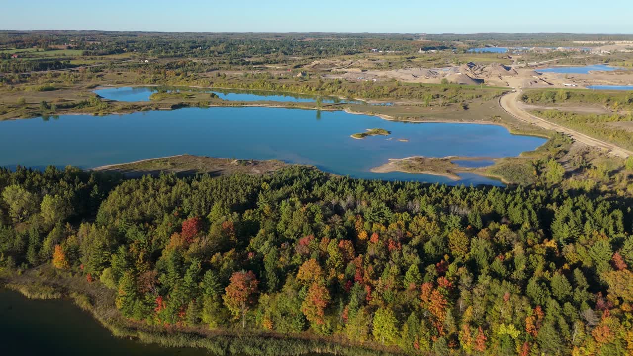 Drone push-in over autumn forest and blue lake at Caledon gravel pit in Ontario