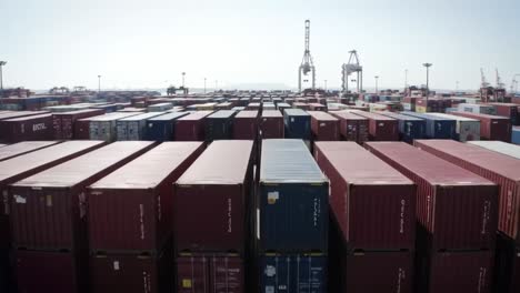 a vast array of shipping containers fills the port under clear blue skies, showcasing the bustling activity of freight movement and logistics. cranes operate above, highlighting the scale of trade.
