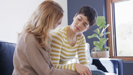 Feliz-Pareja-De-Lesbianas-Caucásicas-Sentadas-En-El-Sofá,-Abrazándose-Y-Apoyándose-Mutuamente-En-Una-Casa-Soleada