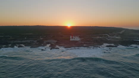 cloudless orange sunrise sky over coastal lighthouse aerial view. foamy ocean