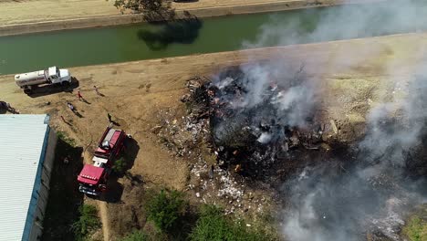 firefighters and firetruck controlling a burnt down building fire at a river, in brazil, south america - aerial drone view