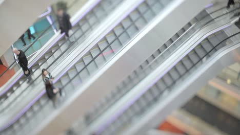 personas en movimiento en escaleras mecánicas en el centro comercial moderno. disparo con lente de cambio de inclinación con profundidad de campo súper superficial.