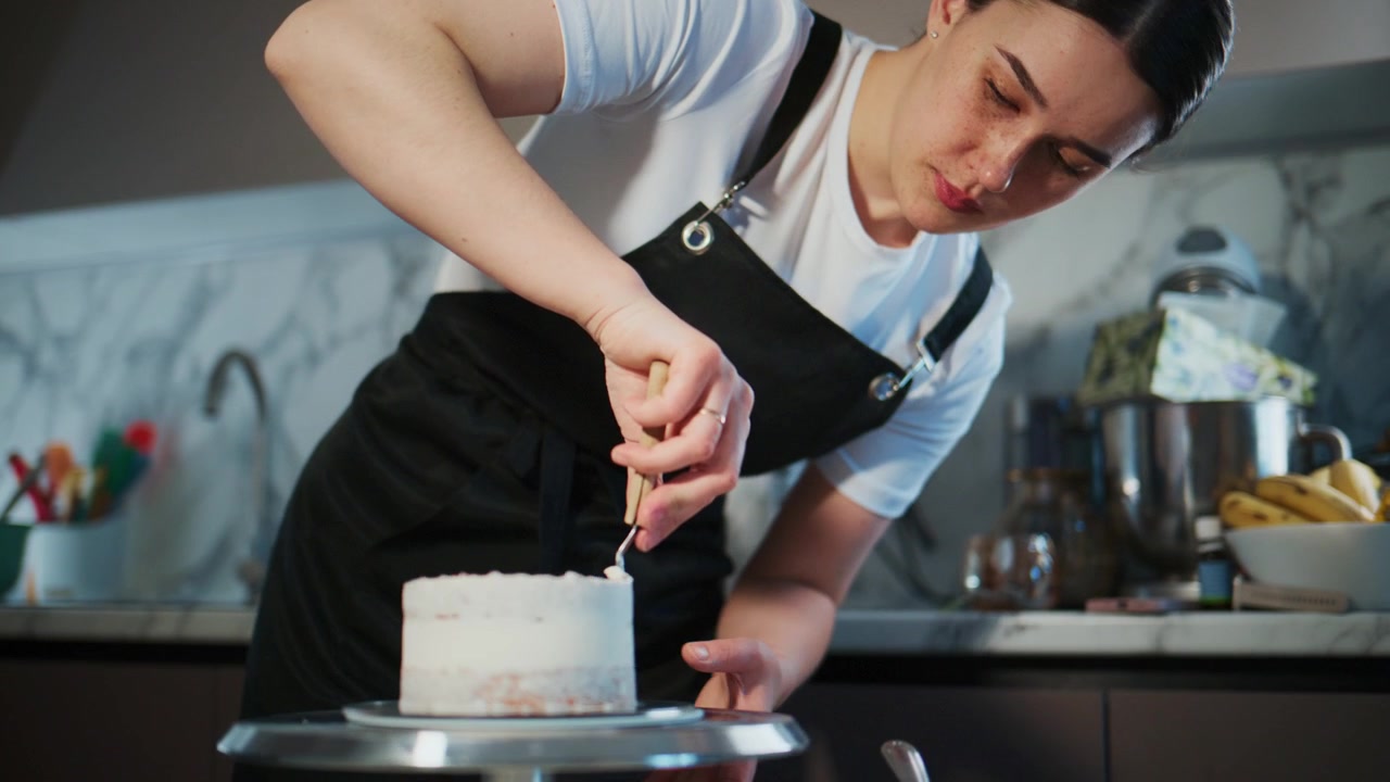 Fokusert person dekorerer forsiktig en kake. De konsentrerer seg om å glatte ut glasur med presisjon. Rolig, dyktig håndverk på et kjøkken. Ideelt for oppskrifter, bakeopplæringer eller dessertmerkevarebygging.