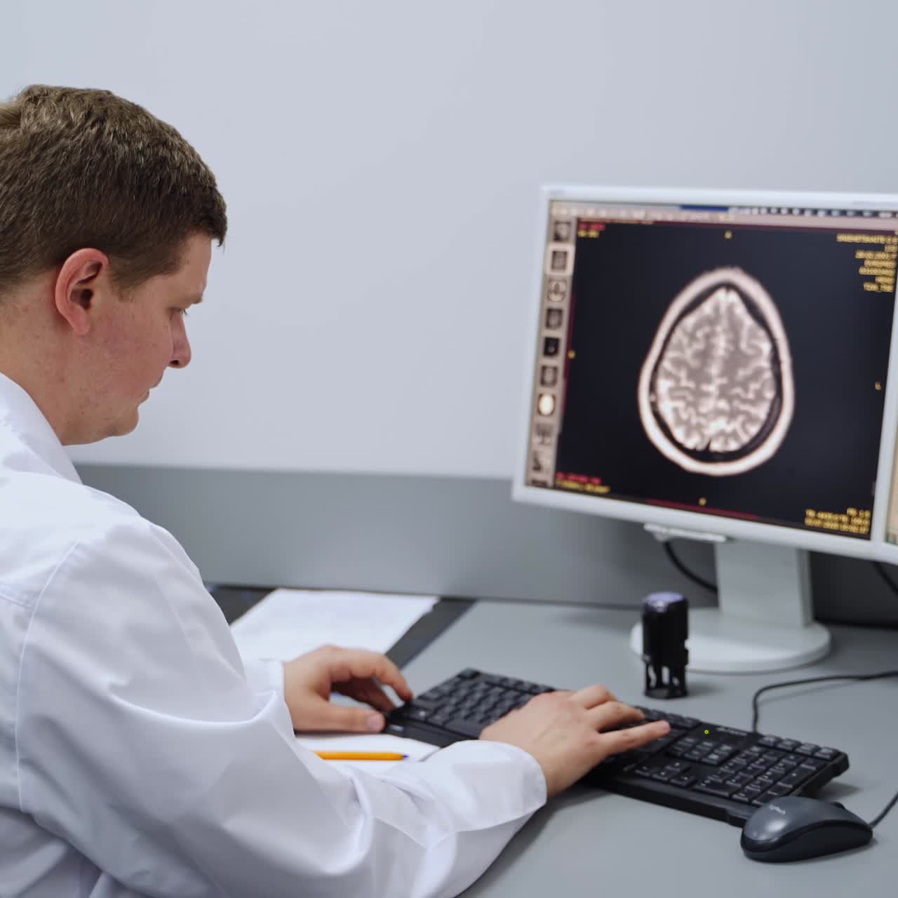 Male doctor sitting at the computer screen typing. Medic describing the MRI head scan and making decision about diagnosis