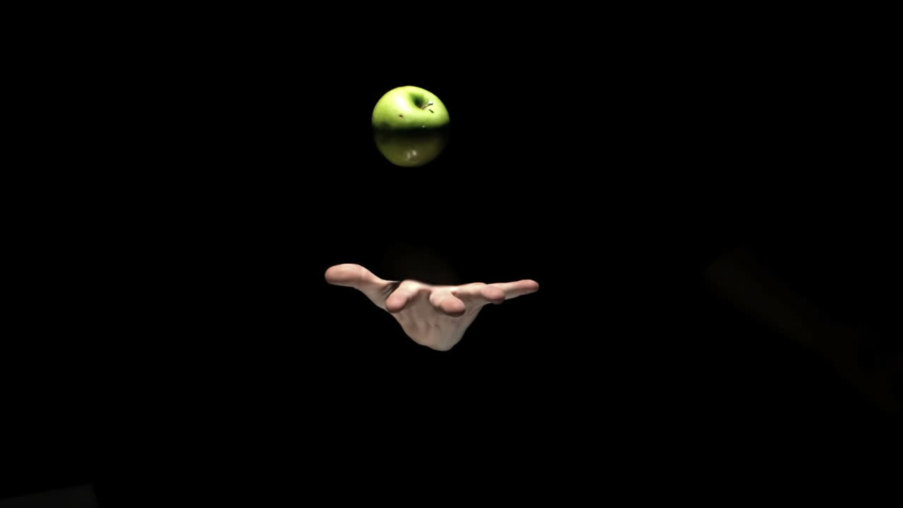 Mano che lancia una mela verde su sfondo nero