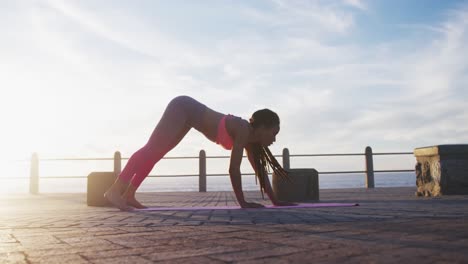 mujer afroamericana en ropa deportiva haciendo yoga en el paseo marítimo