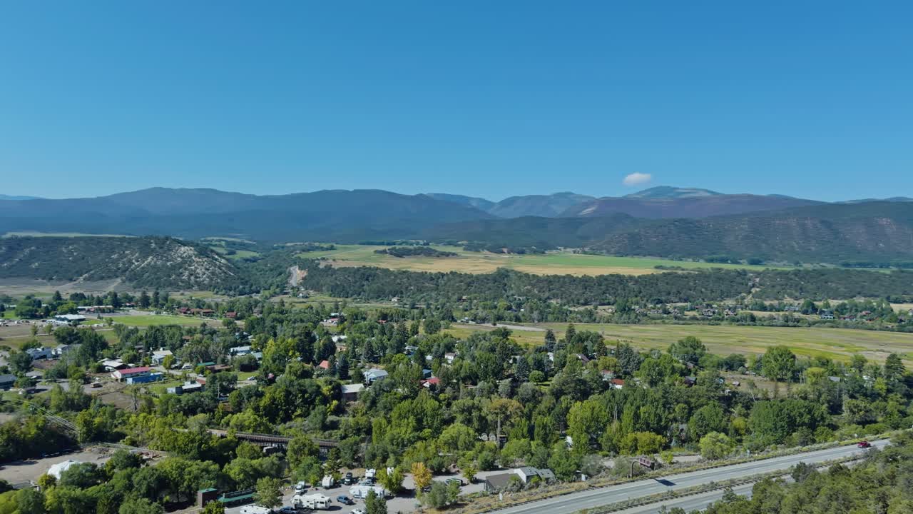 Town of Carbondale nestled in mountain valley under bright sky, establishing pan above neighborhood and fields
