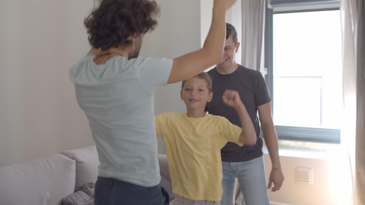 Cheerful excited gay parents and kid having fun at home