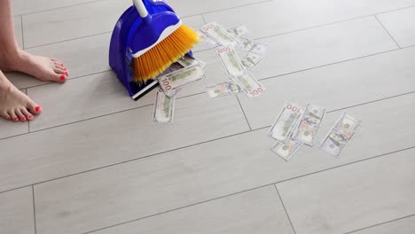 person sweeping us hundred dollar bills into a dustpan