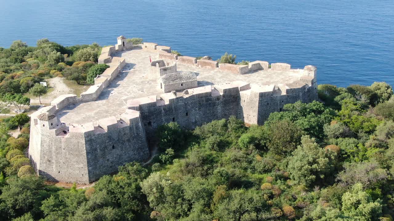 Vista drone in Albania che sorvola un forte medievale su un'isola verde sopra un oceano blu e limpido in una giornata di sole