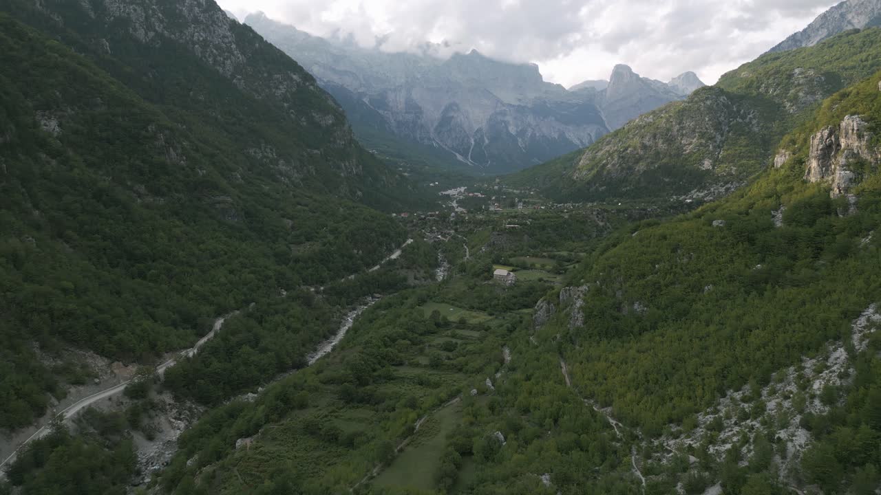Theth Valley in Albania with lush green hills, scattered homes, and winding roads under cloudy skies