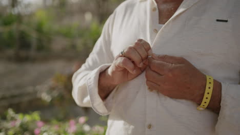 A-mature-man-buttons-up-his-white-shirt-from-the-bottom-up,-getting-ready-for-his-date