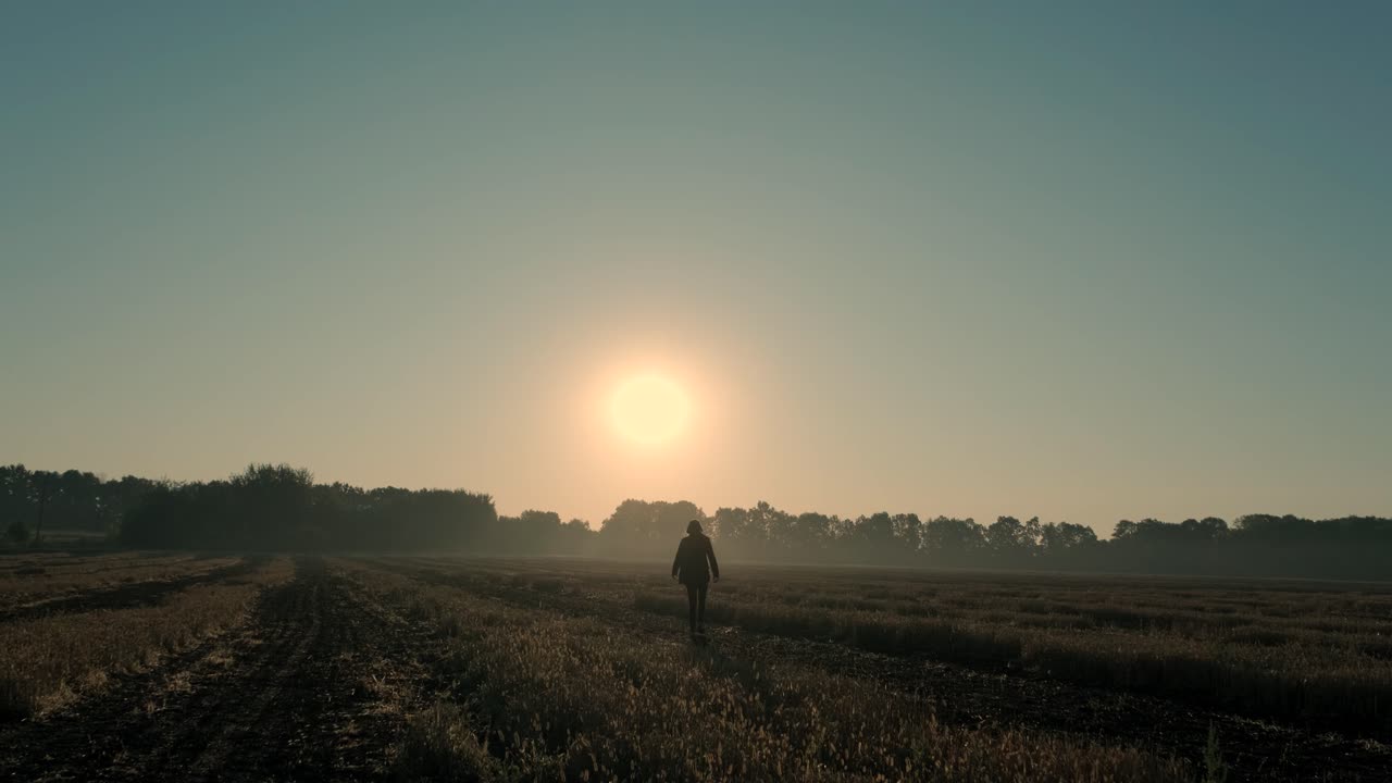 un hombre camina a través de un campo quemado al amanecer y al atardecer. silueta