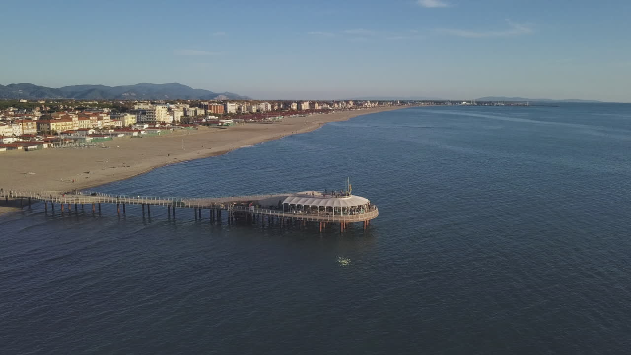 Pier reflecting over the Sea during a Breathtaking Sunset with Town and Hills on the Background