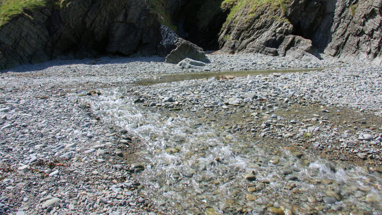 Wide shot of the river Tydu flowing over pebbles and rocks on at Cwmtydu beach
