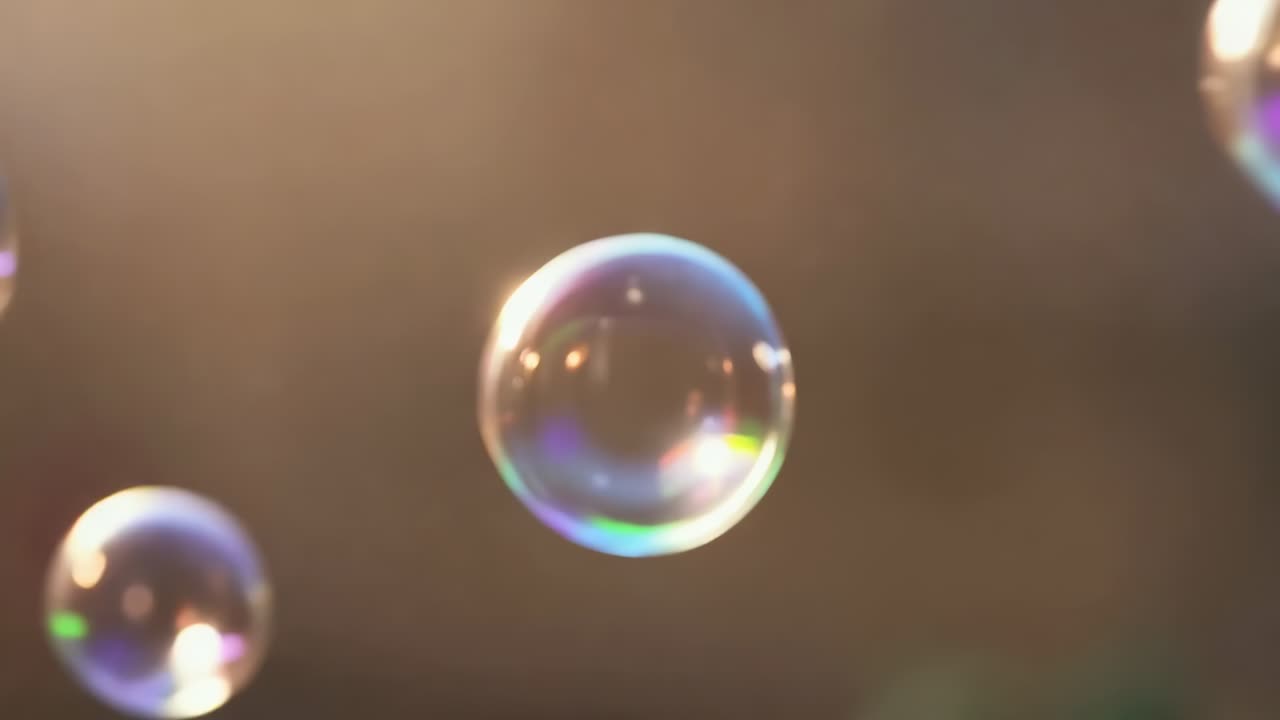 Drifting translucent soap bubbles coming from left, merging to form LOVE in backlight, rupturing