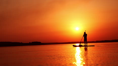 male figure standing on the sup board on calm river. man spending time on water at sunset in summer.