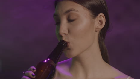 目を閉じてビールを飲み、ディスコで踊る美しい少女の接写