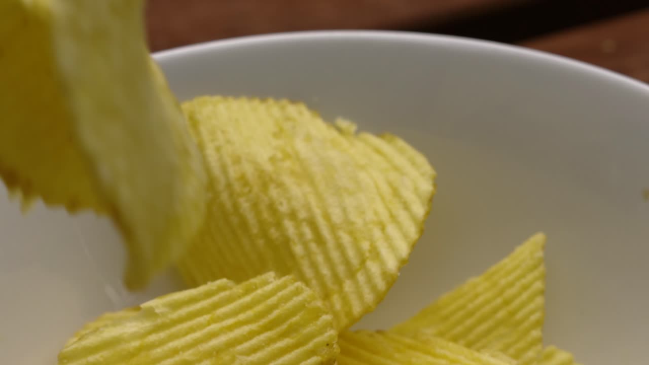 Crinkle Cut Potato Chips Crisps Falling Past Camera into White Bowl on Picnic Table in Slow Motion - 4K Food Clip