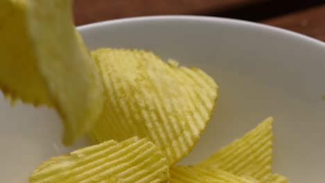 Gewellte-Kartoffelchips-Fallen-In-Zeitlupe-An-Der-Kamera-Vorbei-In-Eine-Weiße-Schüssel-Auf-Einem-Picknicktisch-–-4K-Food-Clip