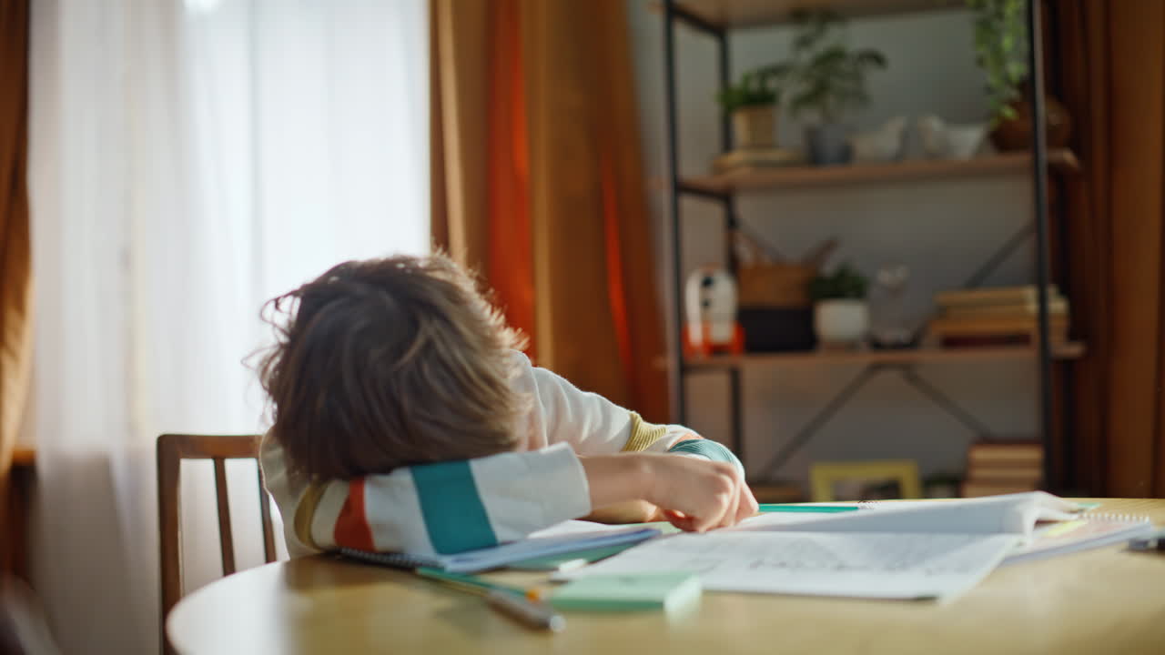 Unmotivated pupil reading textbook doing homework sitting home kitchen closeup