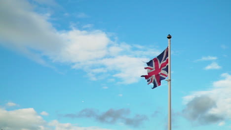 old ripped union jack flag blowing in slow motion against blue sky