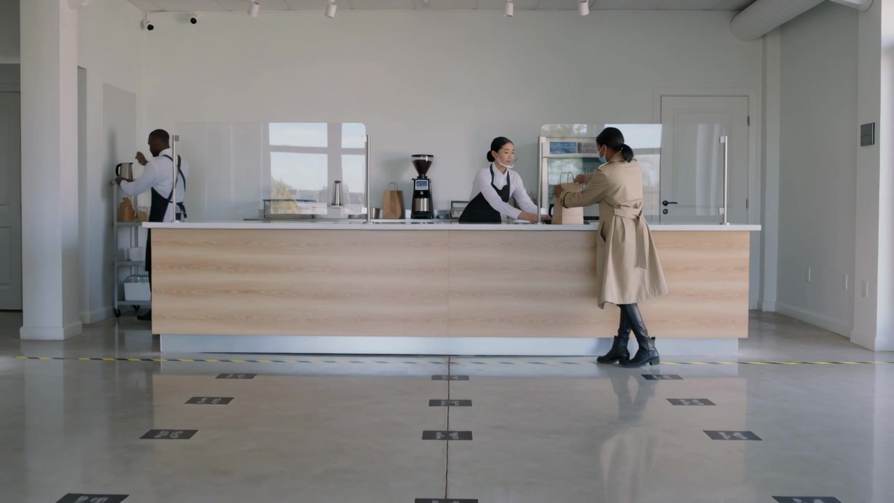 Barista con grembiule che posiziona un sacchetto di carta sul bancone del caffè, mentre il cliente ritira l'ordine.