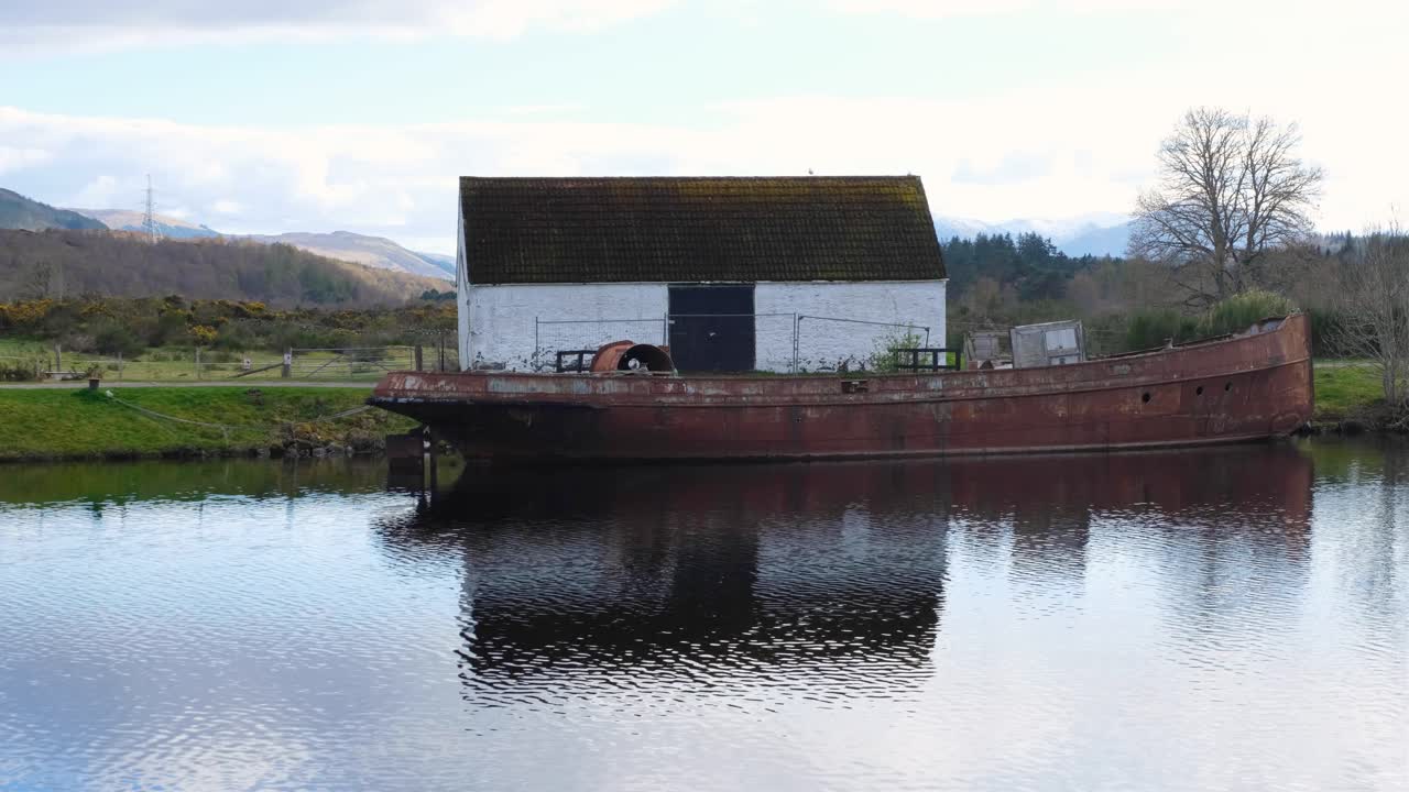 Naturskjønn utsikt over Caledonian Canal, en gammel forlatt lekterbåt og en tradisjonell steinhytte, i Fort Augustus, det skotske høylandet, Storbritannia.