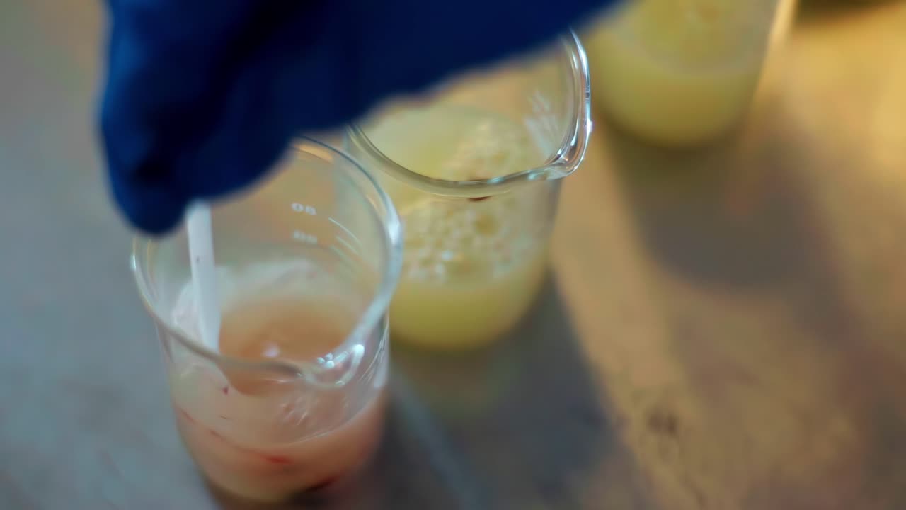 Vista superior de un científico de alimentos con guantes mezclando un líquido viscoso y espeso en un vaso de laboratorio