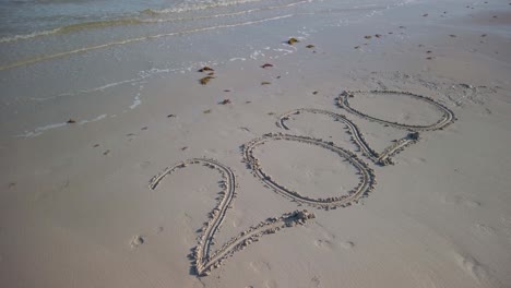 veinte veinte escrito en la arena y en ángulo en una playa