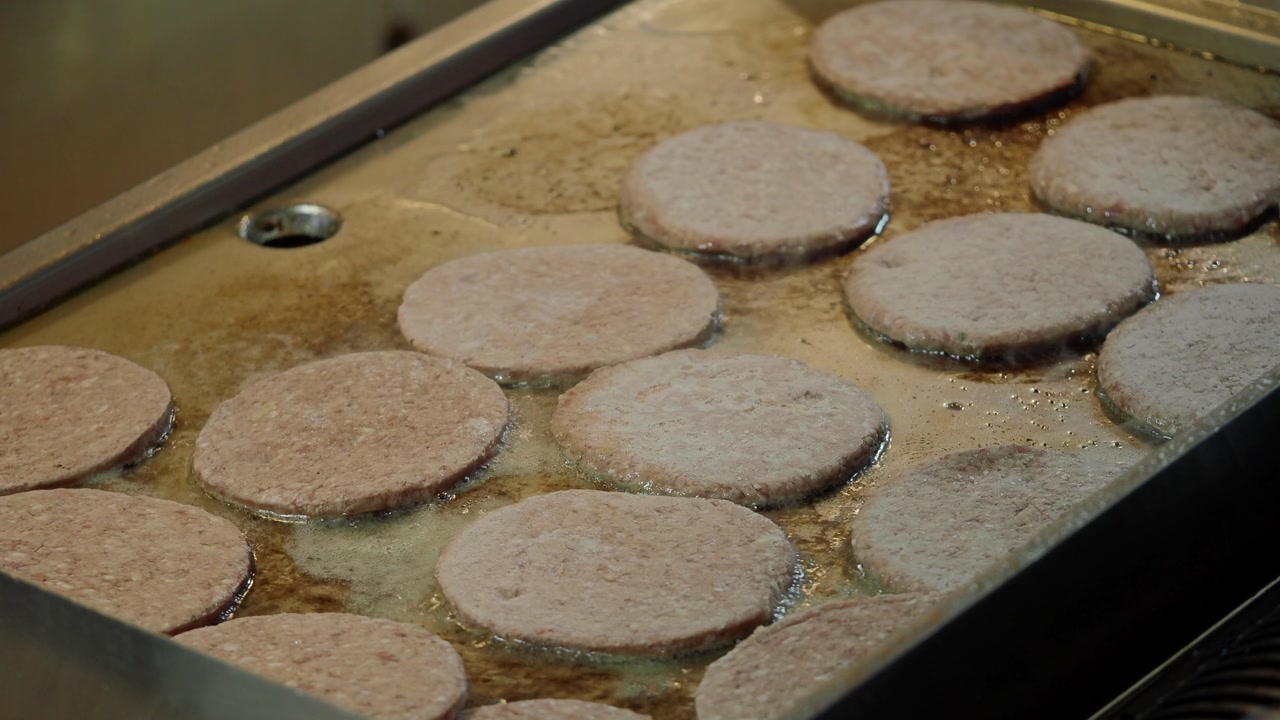 Raw Burger Patties Frying on a Hot Commercial Griddle
