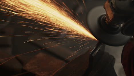 las chispas vuelan mientras la amoladora angular muele metal en el taller de herrería en un banco