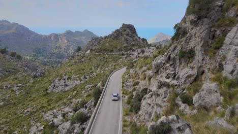 Disparo-De-Un-Dron-Desde-Atrás-Siguiendo-A-Un-Coche-En-Una-Carretera-De-Montaña-Ventosa-En-Sa-Calobra,-Mallorca,-España