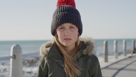 retrato de una niña caucásica linda que parece seria con ropa cálida con un gorro en la playa contemplativa niño en cámara lenta