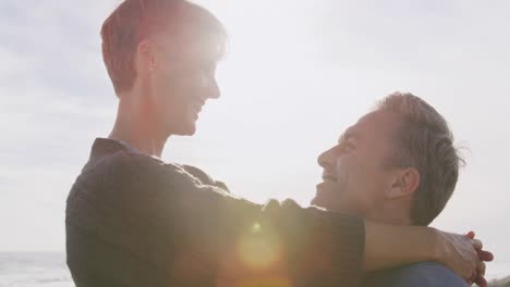 caucasian couple enjoying free time by sea on sunny day embracing and smiling