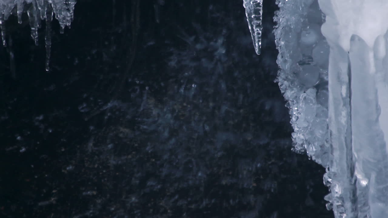 Melting icicles on background of waterfall in spring. Transparent icicles