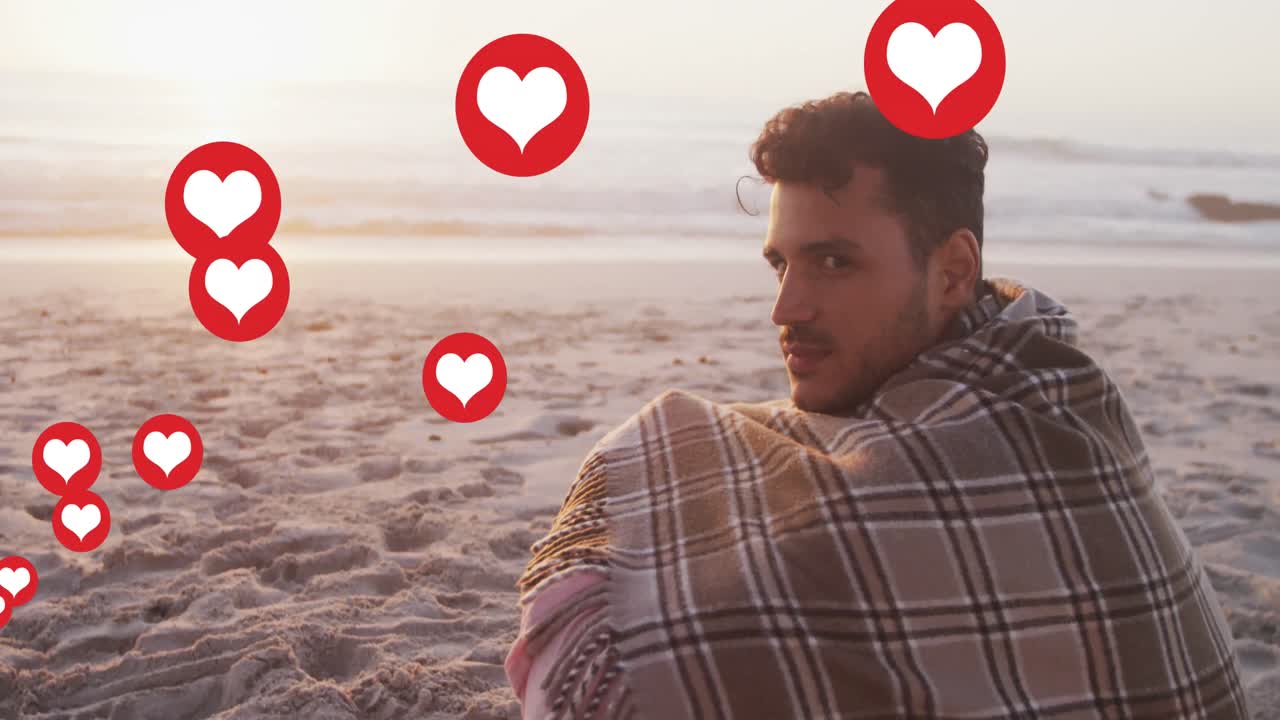 여러 개의 심장 아이콘이 해변에서 미소 짓는 담요로 백인 남자의 초상화에 대해 떠다니고 있습니다.