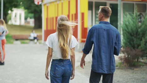 the guy and the girl are walking in the park, talking. the guy is holding a scooter in his hand. happy walk. romantic date