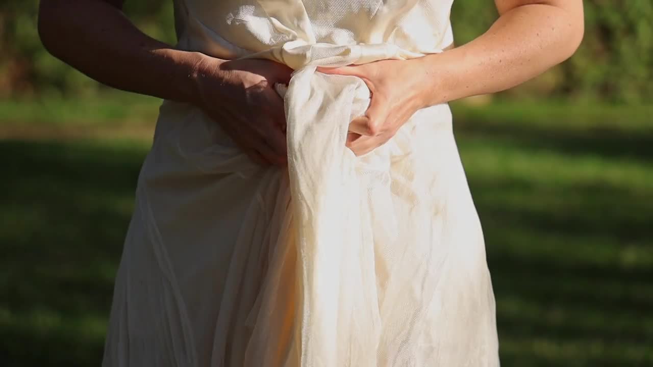Tilt up shot of womans hands holding and lifting skirt of strapless dress up to belly