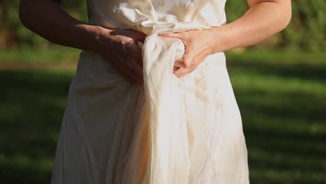 tilt up shot of womans hands holding and lifting skirt of strapless dress up to belly