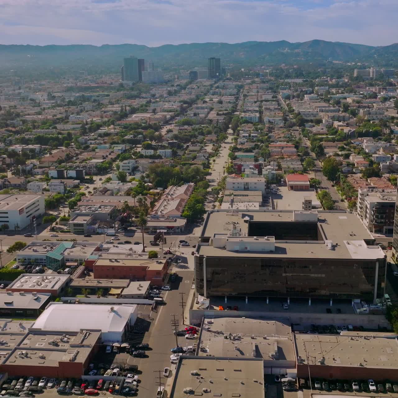 Few multi-storied buildings standing out among the low architectural scenery of LA, USA. Drone footage over the sunny metropolis at daytime