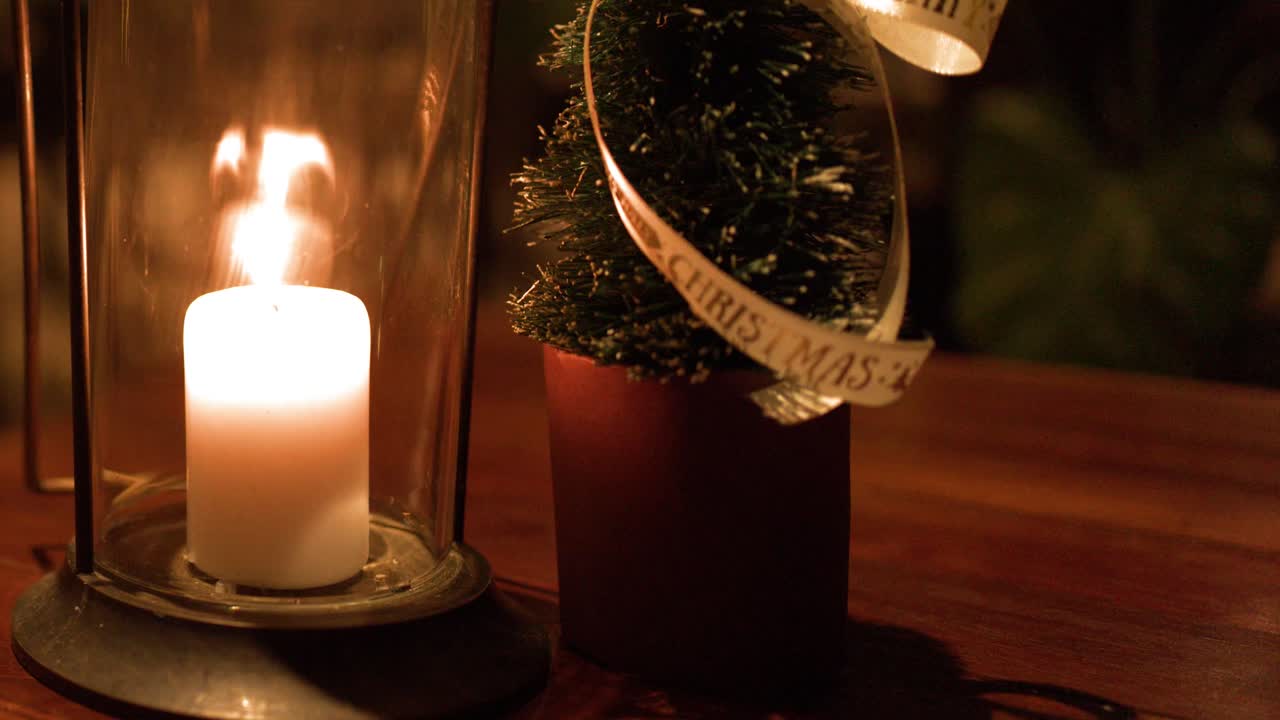 A white pillar candle burns inside a glass hurricane lantern on a wooden table
