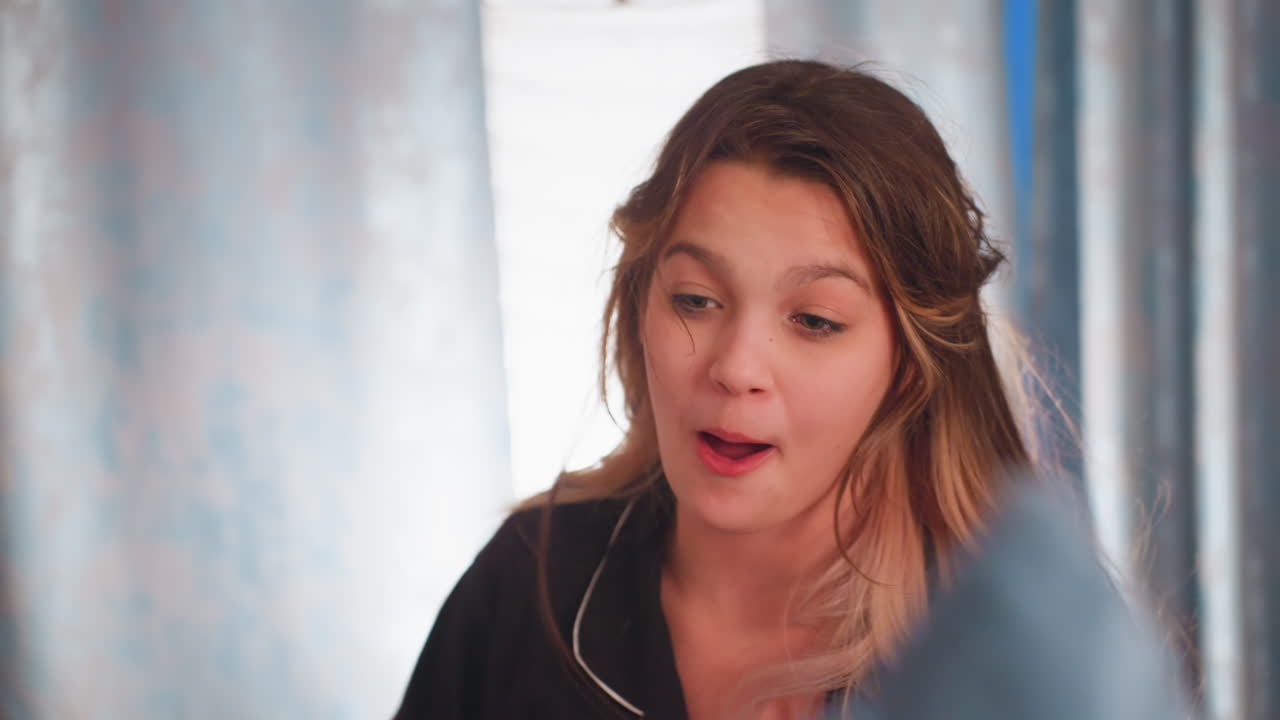 Young girl in black pajamas lifts arm during lively pillow fight with sibling in cozy bedroom, her face shows playful determination, capturing energetic indoor moment filled with joy