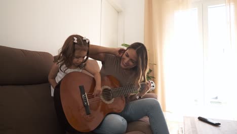 smiling mother and daughter playing guitar on sofa at home